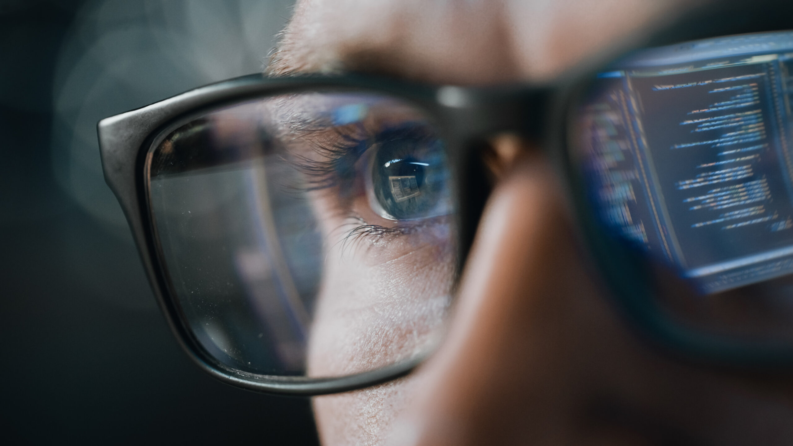 Close-up of a person's eye looking at a computer screen, reflecting a network management interface through their eyeglasses.