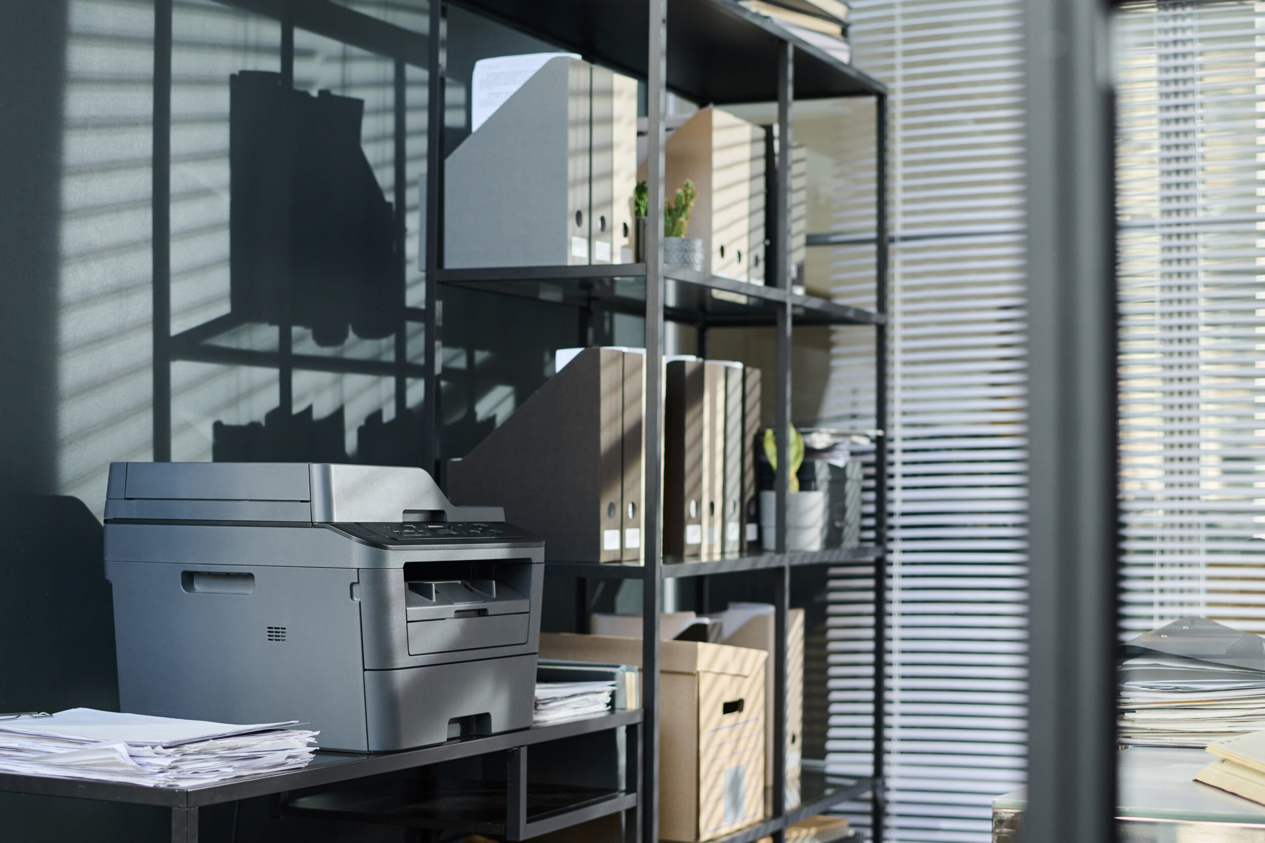 Modern office space with a multifunction printer surrounded by neatly organized shelves filled with files, boxes, and documents, representing an efficient workspace supported by effective print management solutions.