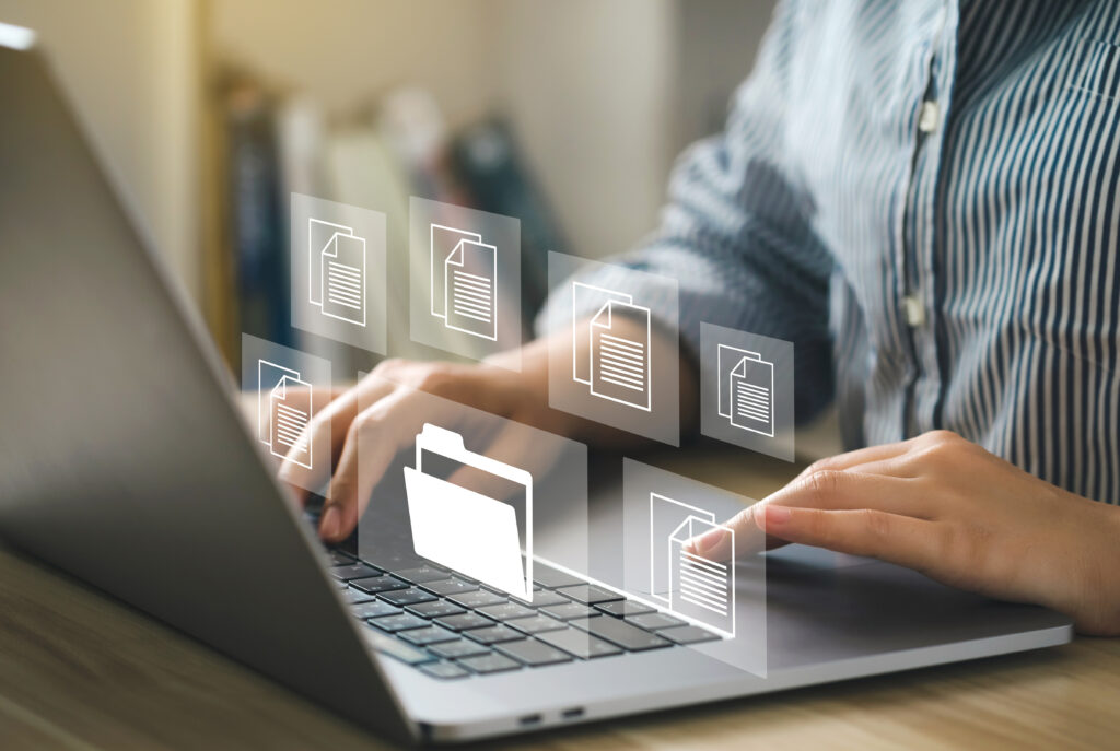 A person uses a laptop with floating digital file and folder icons, representing efficient digital records management for organizing and securing business documents.