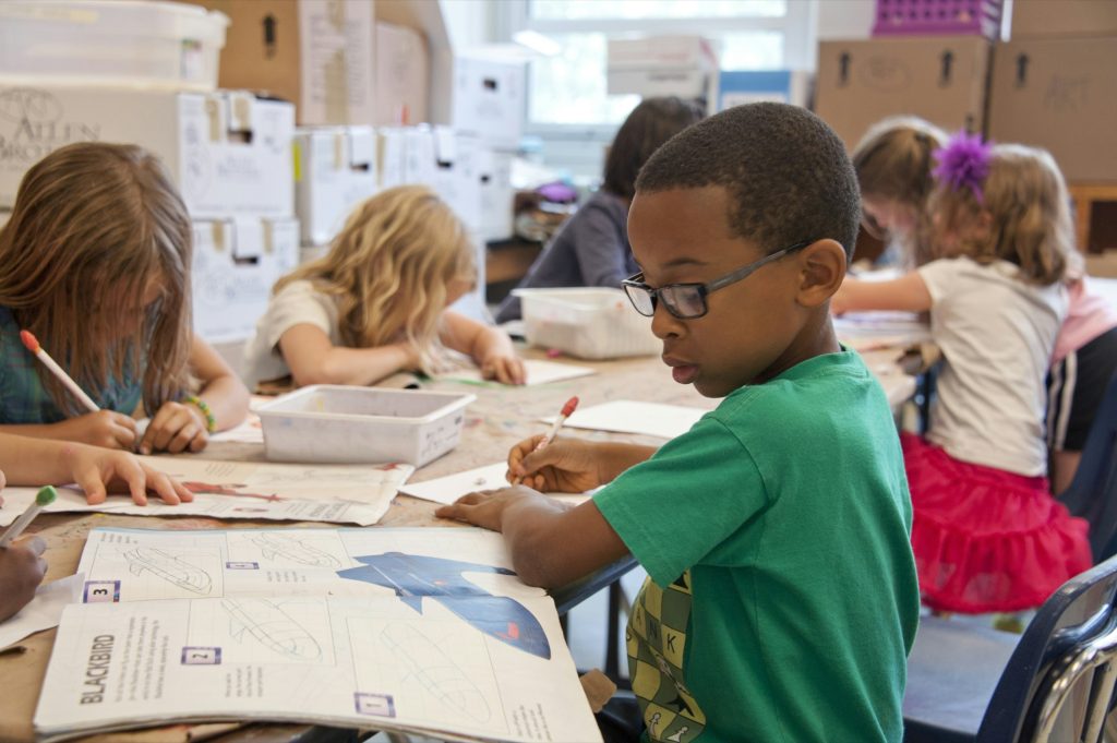 Elementary students working on drawing lessons at a shared classroom table