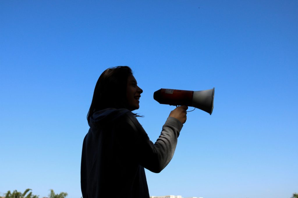 Person speaking into a megaphone against a blue sky