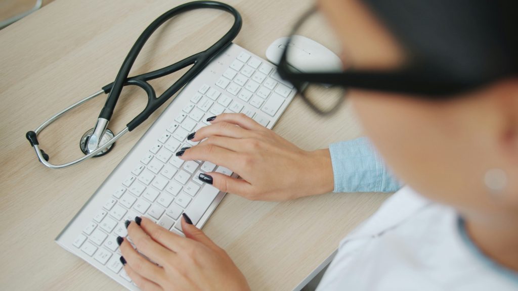 Clinician typing on a keyboard beside a stethoscope