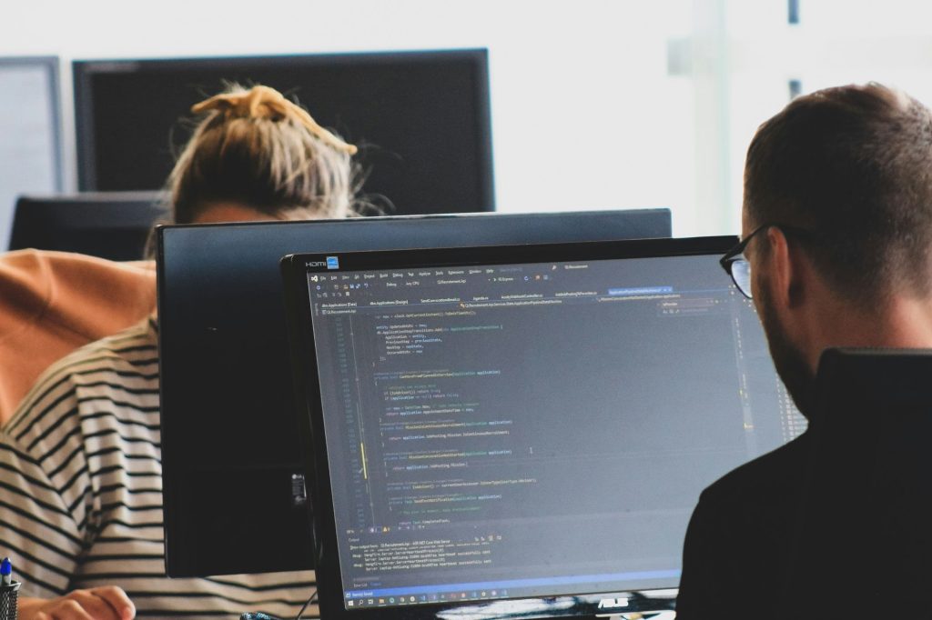 Two IT professionals reviewing code on a desktop monitor